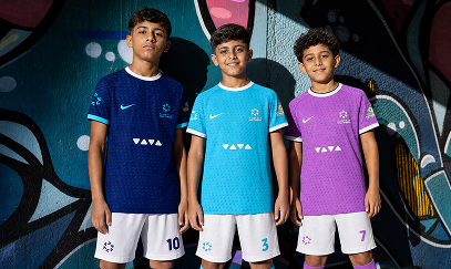 Three young players in football kits standing in front of a painted mural