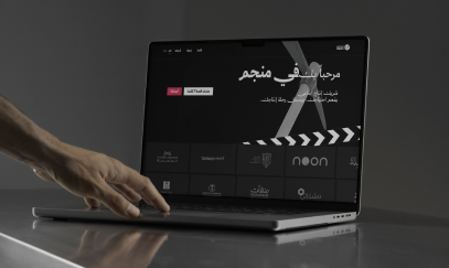 A hand reaching toward a laptop that shows an Arabic website