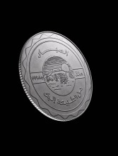 A silver coin with Arabic lettering photographed at an angle on black